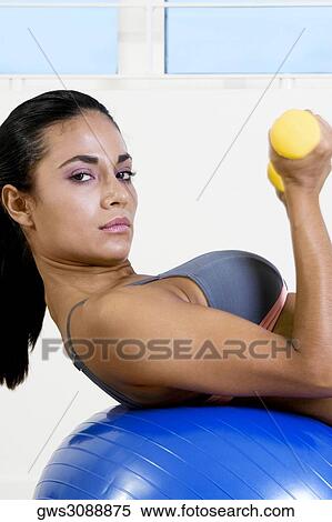 Portrait of a young woman exercising with dumbbells on a fitness ball View Large Photo Image Stock Photography - Portrait of a young woman exercising with dumbbells on a fitness ball. Fotosearch