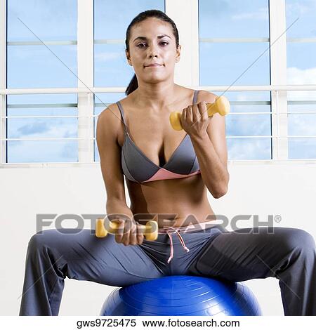 Portrait of a young woman exercising with dumbbells on a fitness ball View Large Photo Image Stock Photography - Portrait of a young woman exercising with dumbbells on a fitness ball. Fotosearch