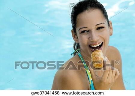 Portrait of a young woman holding a bun close to her mouth View Large Photo Image Stock Photo - Portrait of a young woman holding a bun close to her mouth. Fotosearch