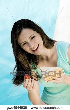 Portrait of a young woman holding a sandwich and a tomato View Large Photo Image Stock Image - Portrait of a young woman holding a sandwich and a tomato. Fotosearch