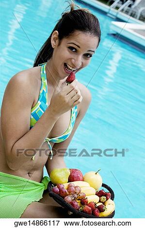 Portrait of a young woman holding a strawberry close to her mouth View Large Photo Image Stock Photo - Portrait of a young woman holding a strawberry close to her mouth. Fotosearch