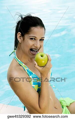Portrait of a young woman holding an apple close to her mouth View Large Photo Image Stock Image - Portrait of a young woman holding an apple close to her mouth. Fotosearch