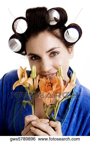 Stock Photograph - Portrait of a young woman with curlers in her hair holding flowers. Fotosearch