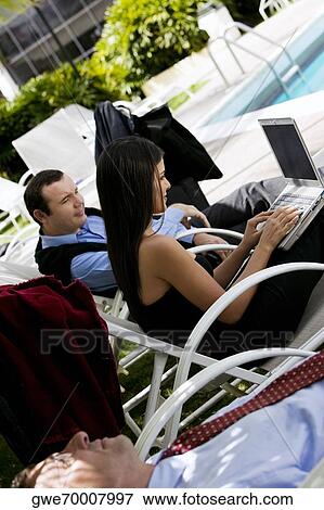 Stock Photo - Side profile of a businesswoman working on a laptop with two businessmen beside her. Fotosearch