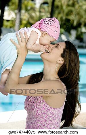 Stock Photography - Side profile of a young woman picking up her daughter. Fotosearch