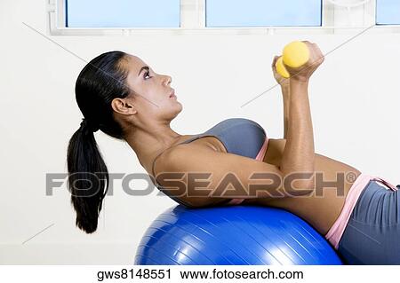 Side profile of a young woman exercising with dumbbells on a fitness ball View Large Photo Image Stock Image - Side profile of a young woman exercising with dumbbells on a fitness ball. Fotosearch