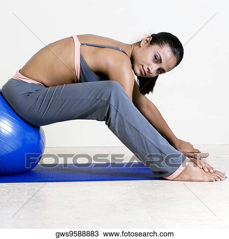 Stock Image - Side profile of a young woman exercising with a fitness ball. Fotosearch