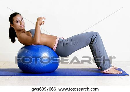 Side profile of a young woman exercising with a fitness ball View Large Photo Image Stock Photograph - Side profile of a young woman exercising with a fitness ball. Fotosearch