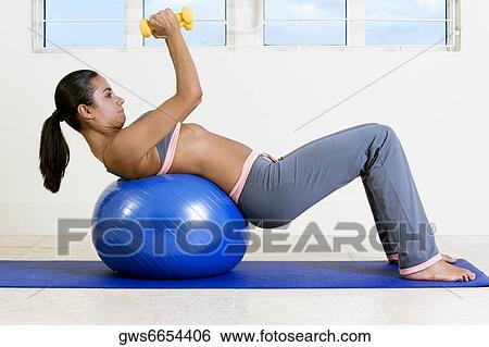 Side profile of a young woman exercising with dumbbells on a fitness ball View Large Photo Image Stock Photograph - Side profile of a young woman exercising with dumbbells on a fitness ball. Fotosearch