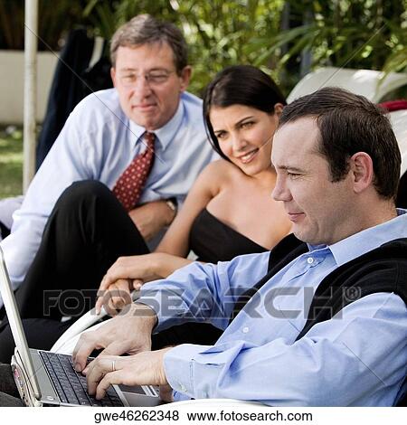 Two businessmen and a businesswoman working on a laptop View Large Photo Image Stock Photo - Two businessmen and a businesswoman working on a laptop. Fotosearch