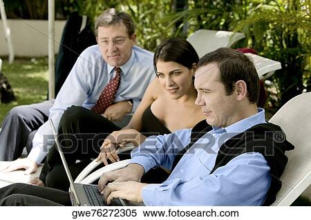 Two businessmen and a businesswoman working on a laptop View Large Photo Image Stock Photography - Two businessmen and a businesswoman working on a laptop. Fotosearch