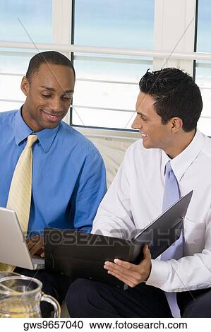 Two businessmen sitting on a couch looking at a file View Large Photo Image Stock Image - Two businessmen sitting on a couch looking at a file. Fotosearch