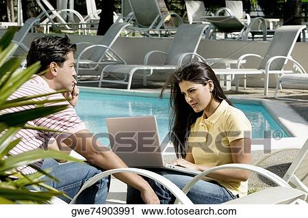 Young woman using a laptop with a young man sitting in front of her View Large Photo Image Stock Image - Young woman using a laptop with a young man sitting in front of her. Fotosearch