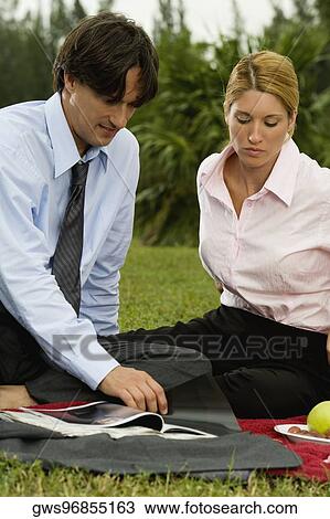 Businessman and a businesswoman reading a magazine in the park View Large Photo Image Stock Image - Businessman and a businesswoman reading a magazine in the park. Fotosearch