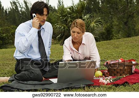 Businessman and a businesswoman sitting in front of a laptop in the park View Large Photo Image Stock Image - Businessman and a businesswoman sitting in front of a laptop in the park. Fotosearch