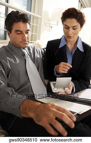 Businesswoman sitting with a businessman holding a calculator View Large Photo Image Stock Image - Businesswoman sitting with a businessman holding a calculator. Fotosearch