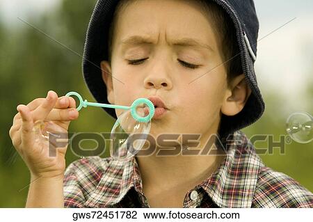 Stock Image - Close-up of a boy blowing bubbles with a bubble wand. Fotosearch