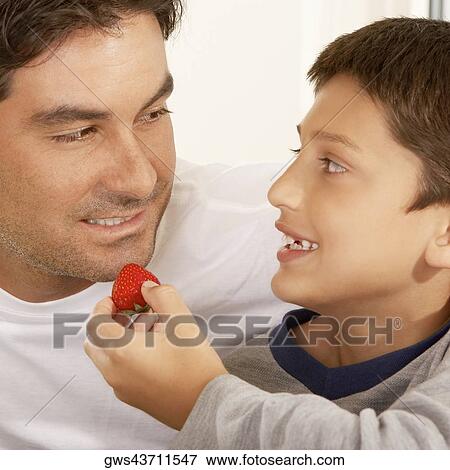 Close-up of a boy feeding his father a strawberry View Large Photo Image Stock Photo - Close-up of a boy feeding his father a strawberry. Fotosearch