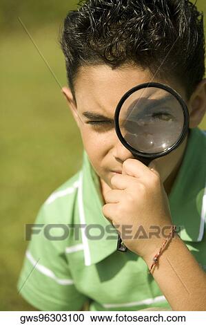 Stock Image - Close-up of a boy looking through a magnifying glass. Fotosearch