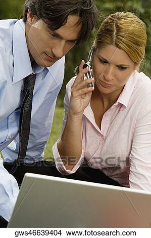 Close-up of a businessman and a businesswoman working on a laptop and talking on a mobile phone View Large Photo Image Picture - Close-up of a businessman and a businesswoman working on a laptop and talking on a mobile phone. Fotosearch
