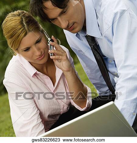 Close-up of a businessman and a businesswoman working on a laptop and talking on a mobile phone View Large Photo Image Stock Image - Close-up of a businessman and a businesswoman working on a laptop and talking on a mobile phone. Fotosearch
