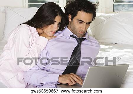 Close-up of a businessman and a businesswoman sitting on the bed using a laptop View Large Photo Image Stock Photo - Close-up of a businessman and a businesswoman sitting on the bed using a laptop. Fotosearch