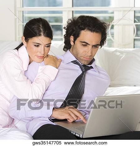Close-up of a businessman and a businesswoman sitting on the bed using a laptop View Large Photo Image Stock Photography - Close-up of a businessman and a businesswoman sitting on the bed using a laptop. Fotosearch