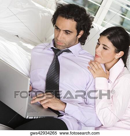 Close-up of a businessman and a businesswoman sitting on the bed using a laptop View Large Photo Image Stock Photography - Close-up of a businessman and a businesswoman sitting on the bed using a laptop. Fotosearch