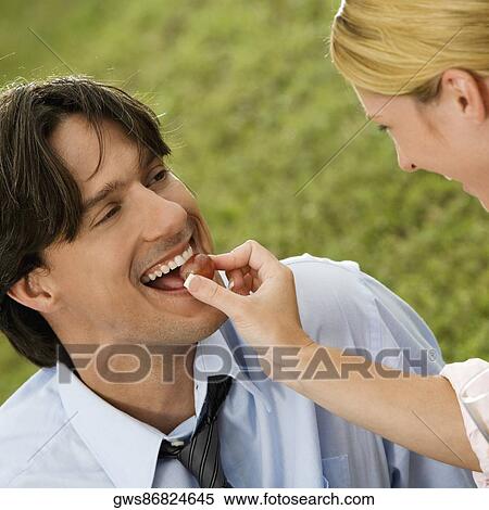 Stock Photography - Close-up of a businesswoman feeding a cherry to a businessman. Fotosearch