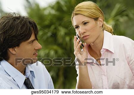Close-up of a businesswoman talking on a mobile phone with a businessman looking at her View Large Photo Image Stock Photo - Close-up of a businesswoman talking on a mobile phone with a businessman looking at her. Fotosearch