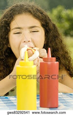 Close-up of a girl eating a burger behind sauce bottles View Large Photo Image Stock Image - Close-up of a girl eating a burger behind sauce bottles. Fotosearch