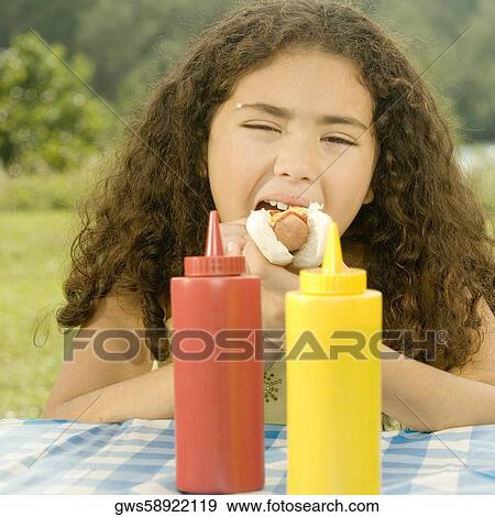 Close-up of a girl eating a burger behind sauce bottles View Large Photo Image Stock Photo - Close-up of a girl eating a burger behind sauce bottles. Fotosearch