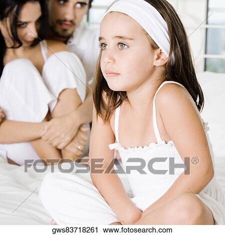 Close-up of a girl sitting on the bed with her parents behind her View Large Photo Image Stock Image - Close-up of a girl sitting on the bed with her parents behind her. Fotosearch