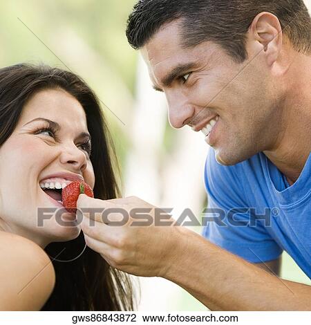 Stock Image - Close-up of a mid adult man feeding a young woman a strawberry. Fotosearch
