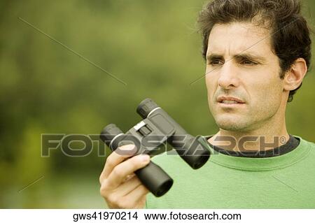 Close-up of a mid adult man holding a pair of binoculars View Large Photo Image Picture - Close-up of a mid adult man holding a pair of binoculars. Fotosearch