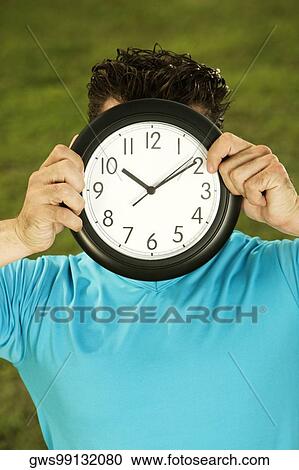Close-up of a mid adult man holding a clock in front of his face View Large Photo Image Stock Image - Close-up of a mid adult man holding a clock in front of his face. Fotosearch