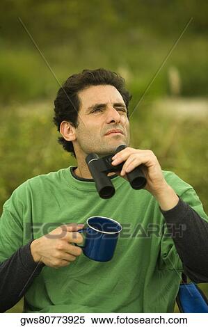 Stock Photography - Close-up of a mid adult man holding a pair of binoculars and a coffee cup. Fotosearch
