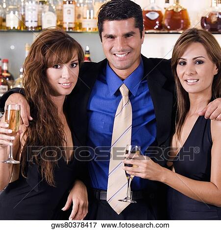 Stock Photo - Close-up of a mid adult man with his arms over two young women. Fotosearch