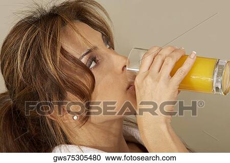 Stock Image - Close-up of a mid adult woman drinking a glass of orange juice. Fotosearch