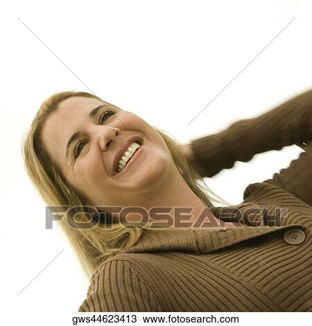 Stock Image - Close-up of a mid adult woman smiling with her hand in her hair. Fotosearch