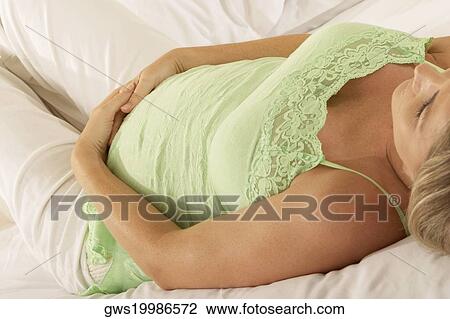 Close-up of a pregnant woman lying on the bed touching her abdomen View Large Photo Image Stock Image - Close-up of a pregnant woman lying on the bed touching her abdomen. Fotosearch