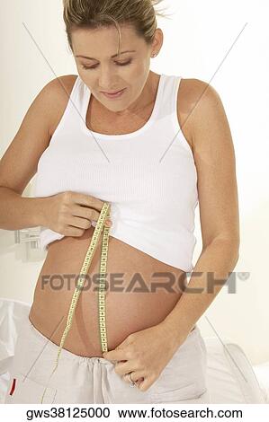 Stock Image - Close-up of a pregnant woman measuring her abdomen with a measuring tape. Fotosearch
