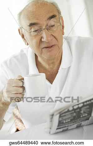 Stock Image - Close-up of a senior man holding a cup of coffee reading a newspaper. Fotosearch
