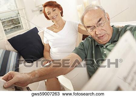 Close-up of a senior man reading a newspaper with a senior woman sitting behind him View Large Photo Image Stock Image - Close-up of a senior man reading a newspaper with a senior woman sitting behind him. Fotosearch
