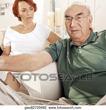 Close-up of a senior man reading a newspaper with a senior woman sitting behind him View Large Photo Image Stock Image - Close-up of a senior man reading a newspaper with a senior woman sitting behind him. Fotosearch