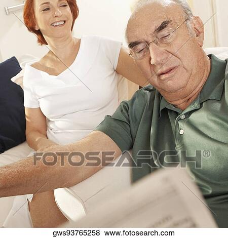 Close-up of a senior man reading a newspaper with a senior woman sitting behind him View Large Photo Image Stock Photo - Close-up of a senior man reading a newspaper with a senior woman sitting behind him. Fotosearch