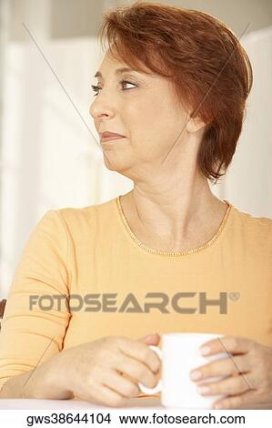 Picture - Close-up of a senior woman holding a cup of coffee looking sideways. Fotosearch