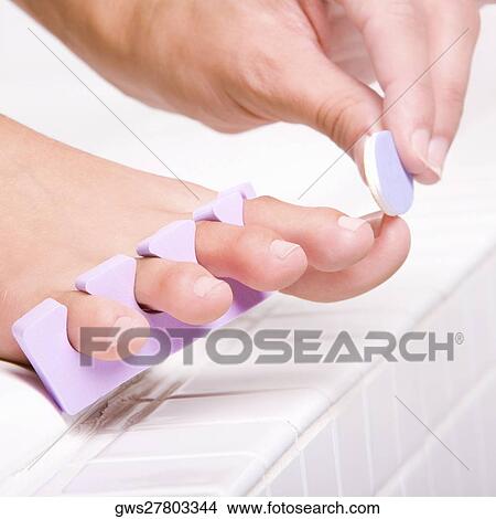 Picture - Close-up of a woman's hand shaping her toenail with a nail file. Fotosearch