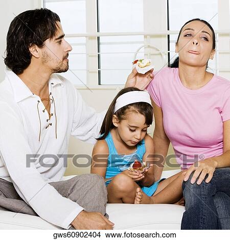 Picture - Close-up of a young couple and their daughter eating a pastry. Fotosearch