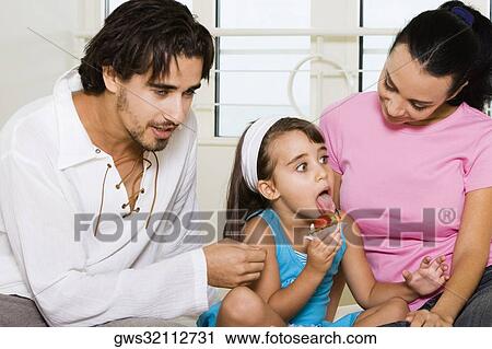 Stock Image - Close-up of a young couple looking at their daughter eating a pastry. Fotosearch